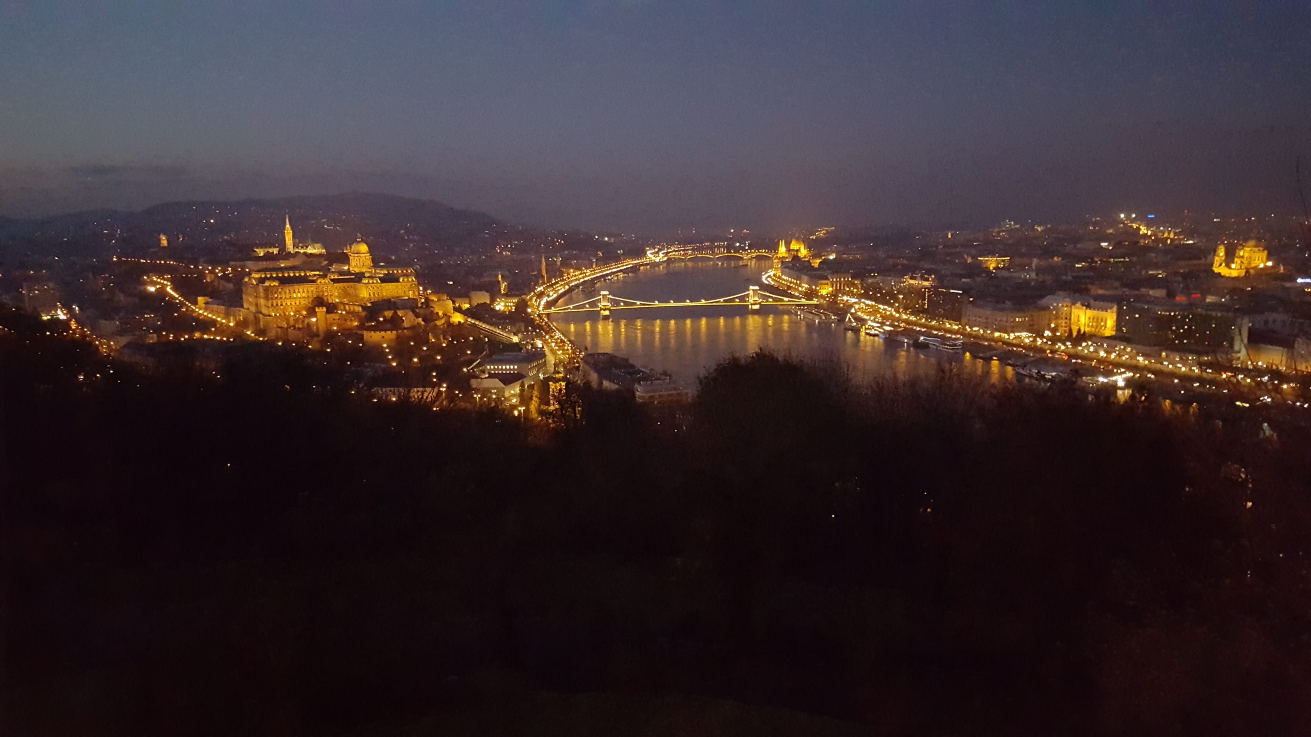 Vista nocturna de Budapest iluminada, con el río Danubio y el Parlamento de fondo.